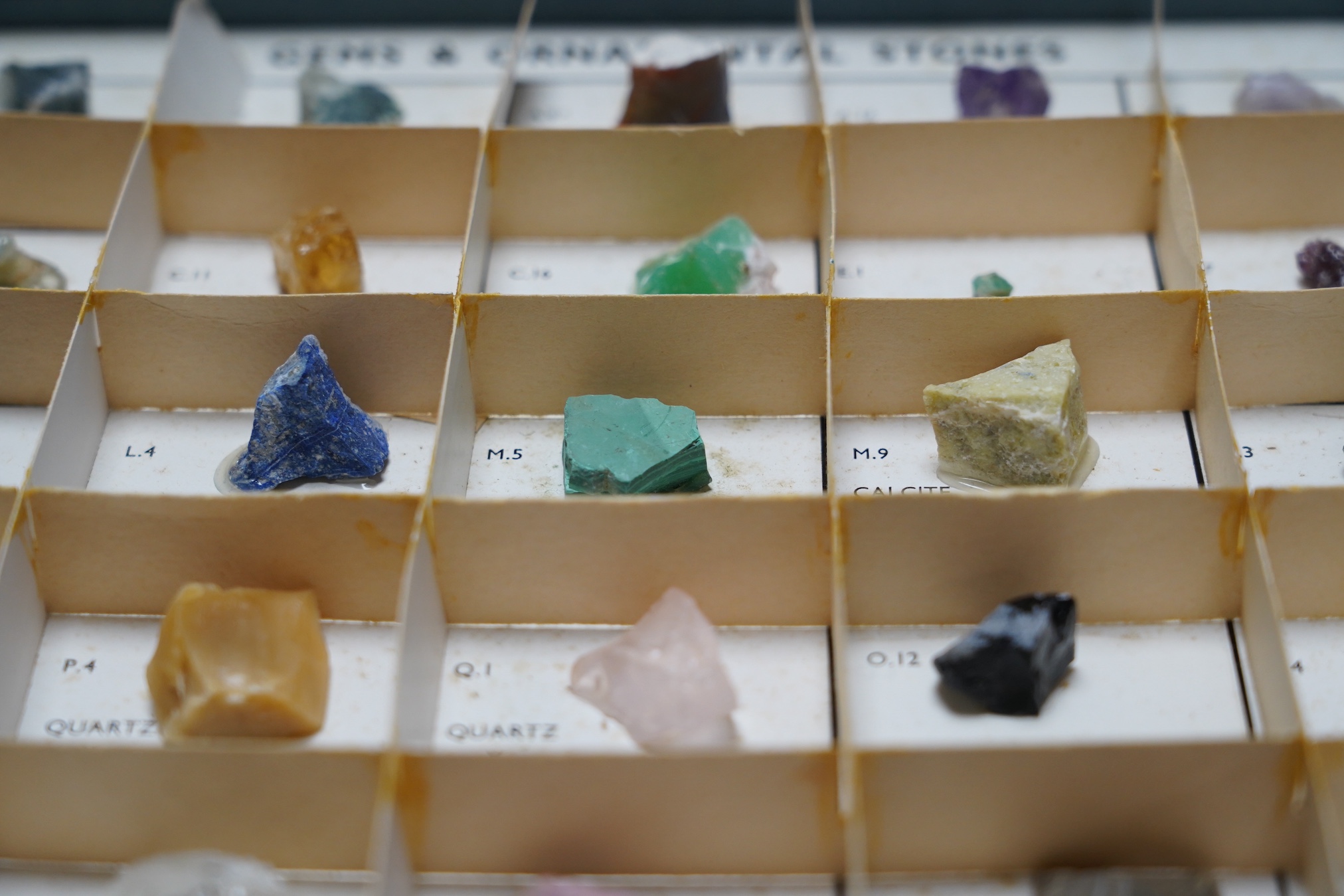 A case of uncut gems and ornamental stones, including diamond, amethyst, nephrite, malachite, rutilated quartz, etc. Fair condition.